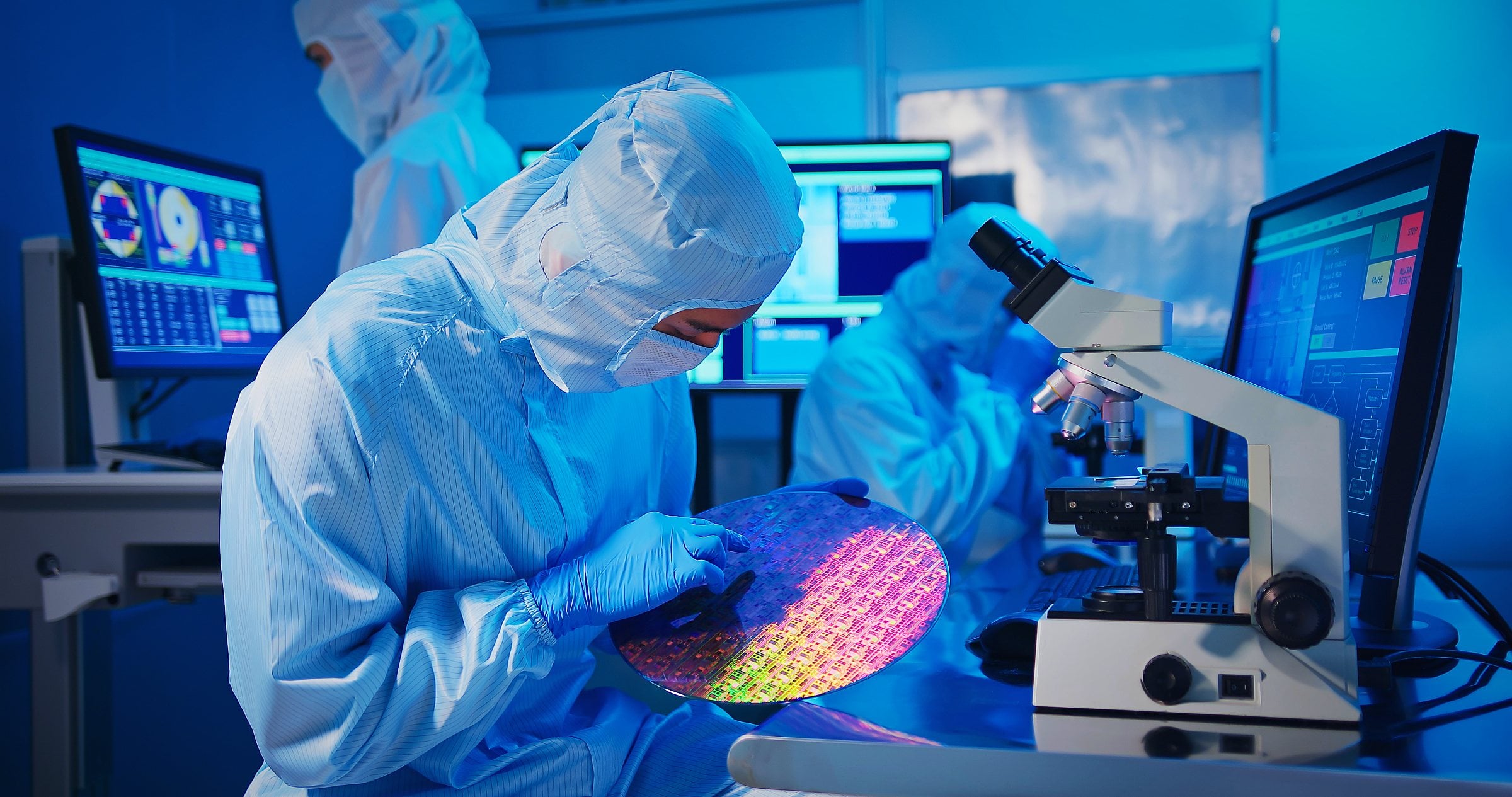 Engineer in a cleanroom suit inspecting a silicon wafer in a semiconductor fab